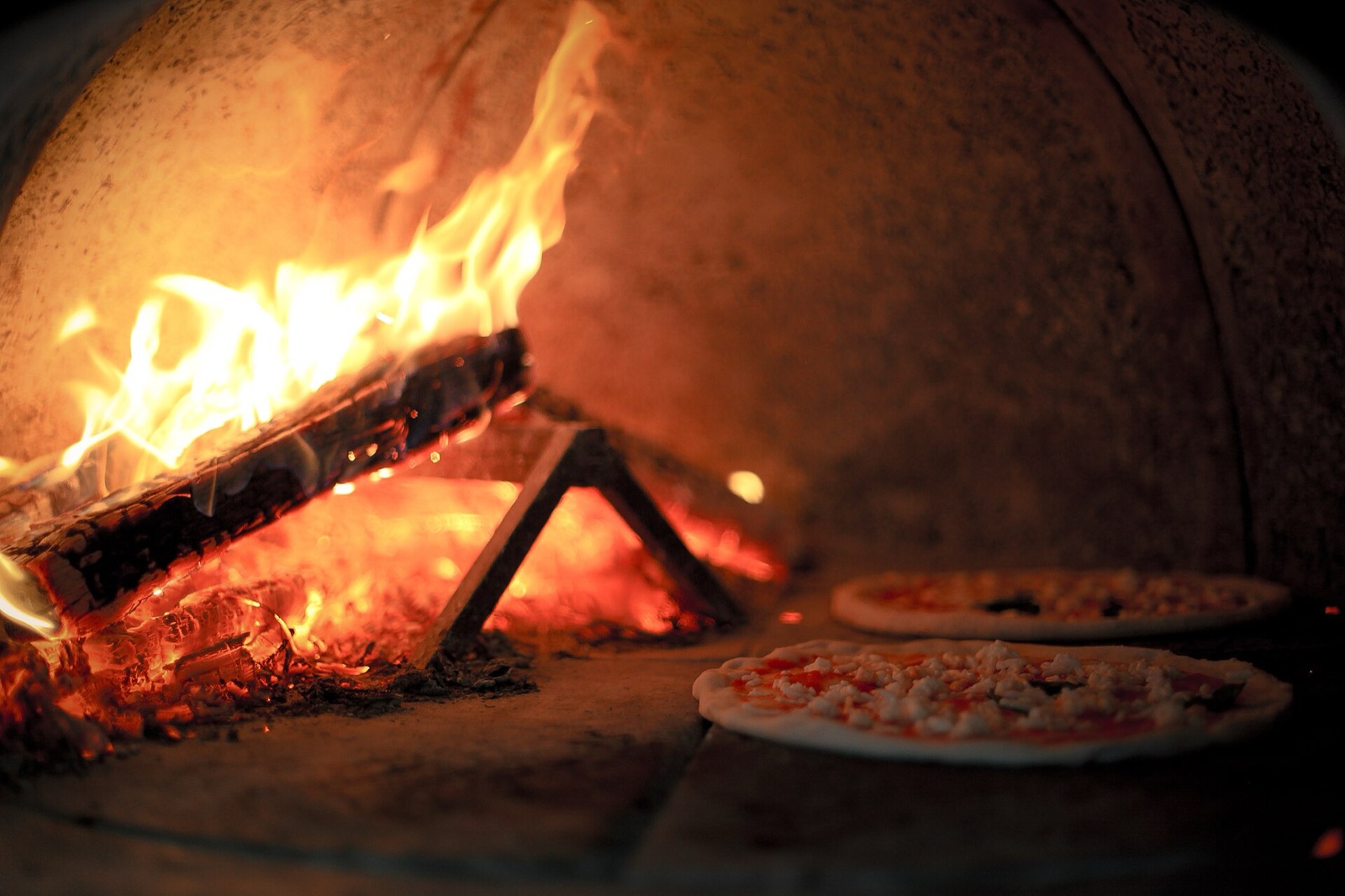 Wood fire burning inside a domed brick pizza oven with two pizzas on the floor