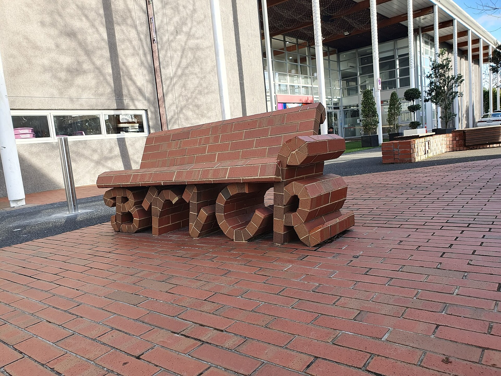 A brick bench whose base is sculpted into lettering, on a brick-paved plaza
