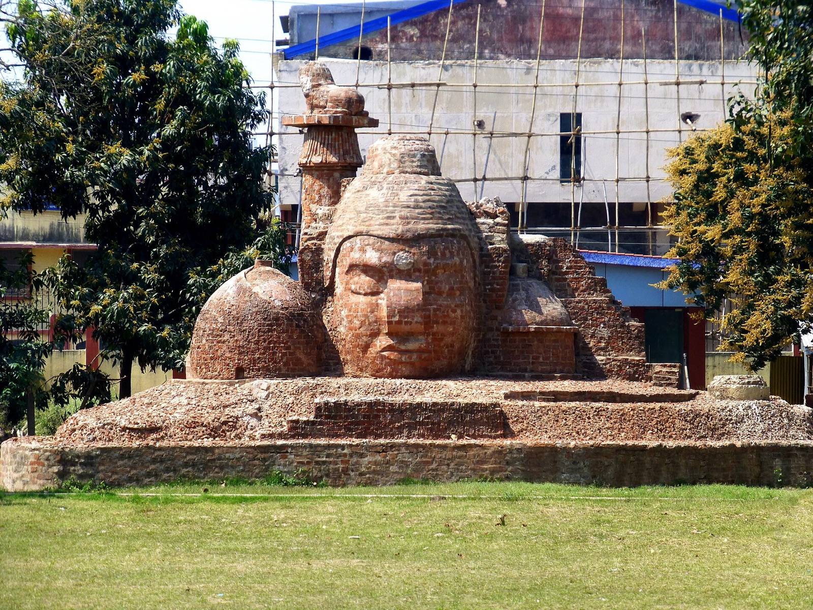 A large head sculpted in fired brick on a low brick platform, with trees behind